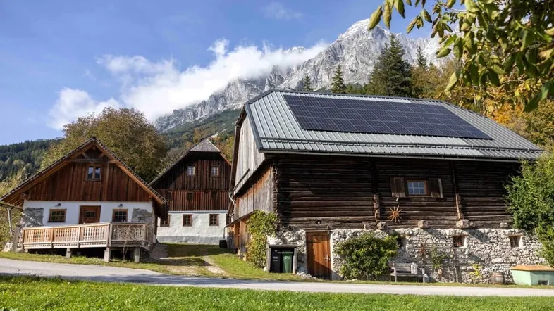 Traditionelle Holzhäuser mit Solaranlage auf dem Dach vor einer beeindruckenden Bergkulisse.
