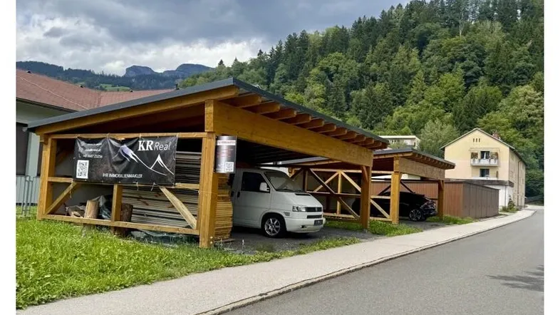 Mehrere Holzcarports bieten geschützten Parkraum für Fahrzeuge in ländlicher Umgebung mit Wald im Hintergrund.