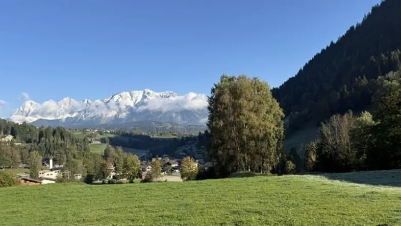 Weitläufige grüne Landschaft mit malerischem Dorf und schneebedeckten Bergen im Hintergrund.