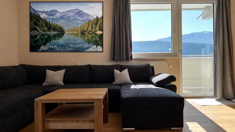 Helles Wohnzimmer mit gemütlichem Sofa, Holztisch und Zugang zum Balkon mit Bergblick.