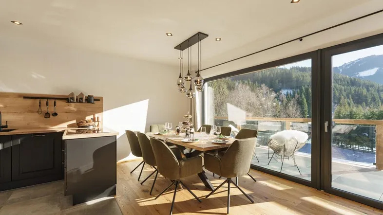 Heller Wohn- und Essbereich mit moderner Küche, Holzboden und großem Fenster mit Bergblick.
