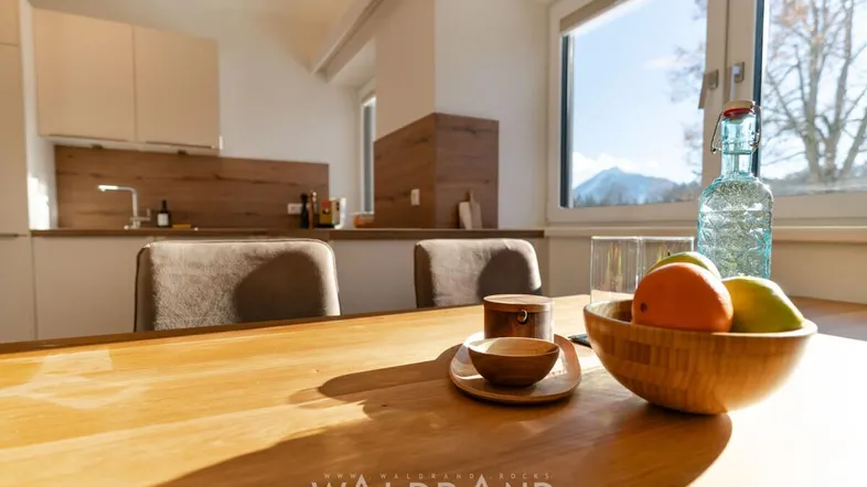 Helle Küche mit Holztisch, modernen Schränken und Blick auf die Berge durch das Fenster.