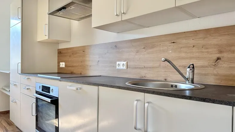 Moderne Einbauküche mit hellen Schränken, dunkler Arbeitsplatte und Holzrückwand.