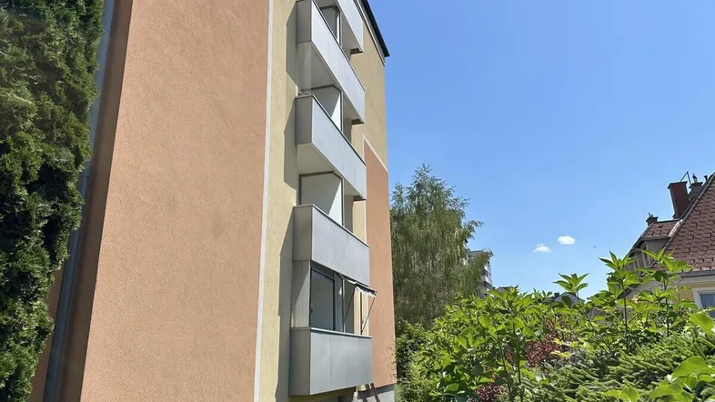 Seitenansicht eines Wohngebäudes mit mehreren Balkonen und üppigem Grün.