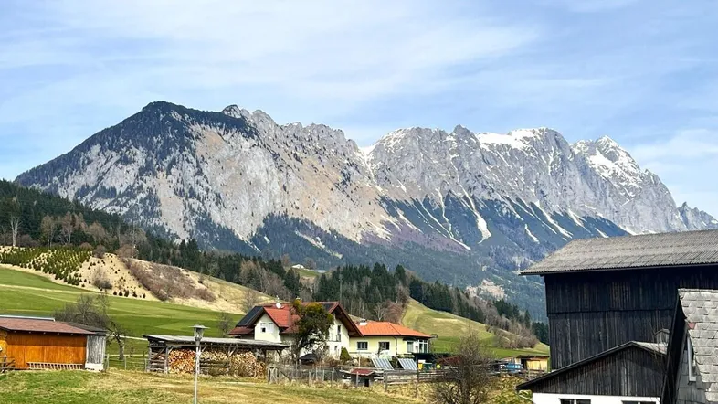 Blick auf eine ländliche Umgebung mit traditionellen Häusern und majestätischen Bergen im Hintergrund.