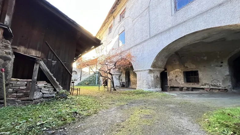 Innenhof eines alten Gebäudes mit unbefestigtem Weg und angrenzenden Nebengebäuden unter hellem Himmel.