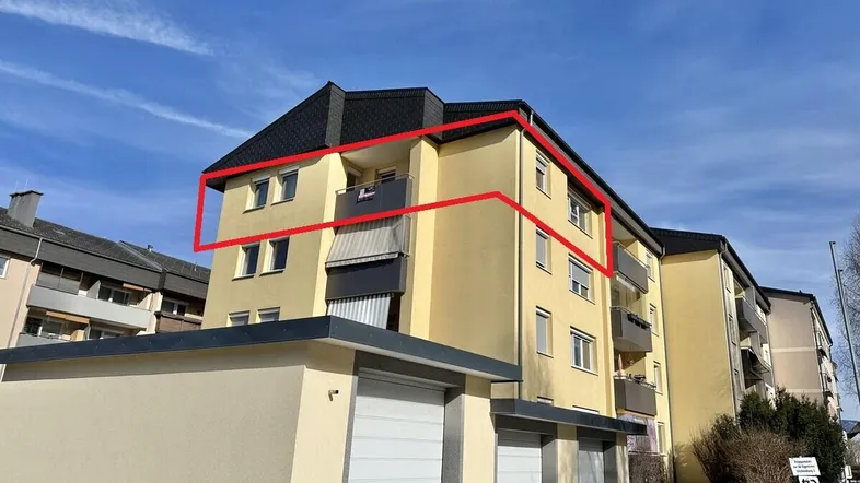 Gelbes Mehrfamilienhaus mit Satteldach und Garagen im Vordergrund unter blauem Himmel.