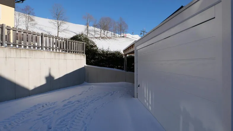 Schneebedeckte Zufahrt zur Garage und zum Carport mit Blick auf die verschneite Landschaft.