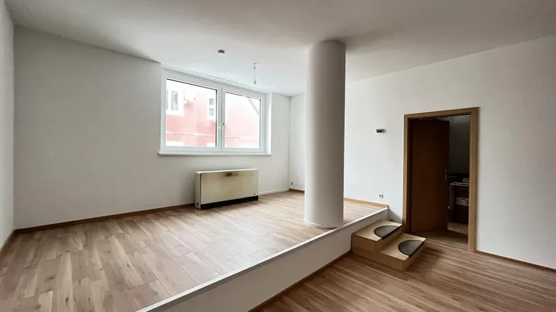 Heller Wohnraum mit Holzfußboden, einer erhöhten Ebene und einem großen Fenster.