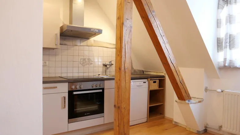Funktionale Küche mit Einbaugeräten, Fliesenrückwand und sichtbarem Holzbalken unter Dachschräge.