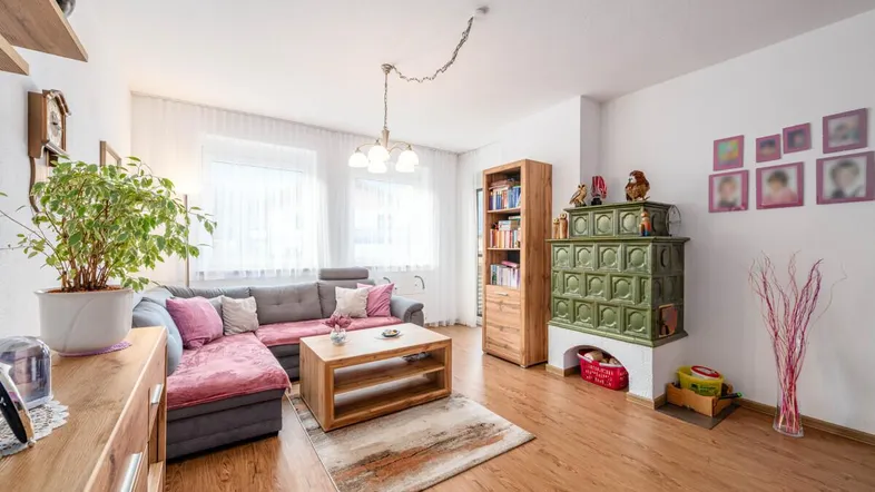 Gemütliches Wohnzimmer mit Kachelofen, Laminatboden und bequemer Eckcouch für entspannte Stunden.