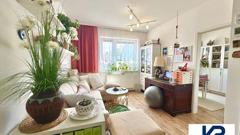 Helles Wohnzimmer mit gemütlicher Sitzecke, Schreibtisch und vielen Pflanzen, ideal zum Entspannen.
