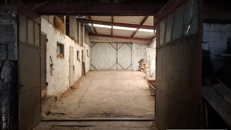 Großer, leerer Raum mit hohen Toren und sichtbaren Holzbalken, ideal als Lager oder Garage.