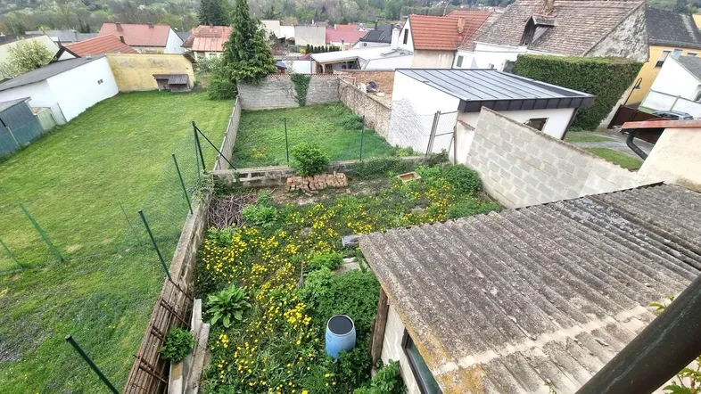 Blick von oben auf einen ungepflegten Gartenbereich mit angrenzenden Häusern und viel Grün.