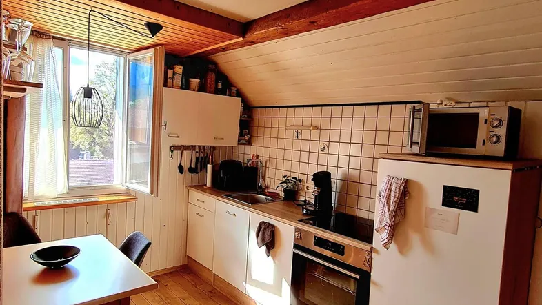 Helle Küche im Dachgeschoss mit Holzboden, weißen Schränken und Essbereich.