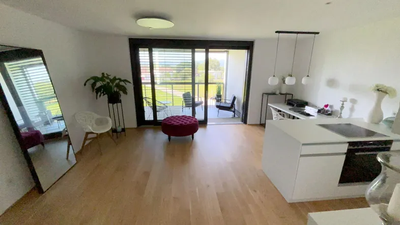 Helles, offenes Wohnzimmer mit integrierter Küche, Holzboden und Zugang zum Balkon.