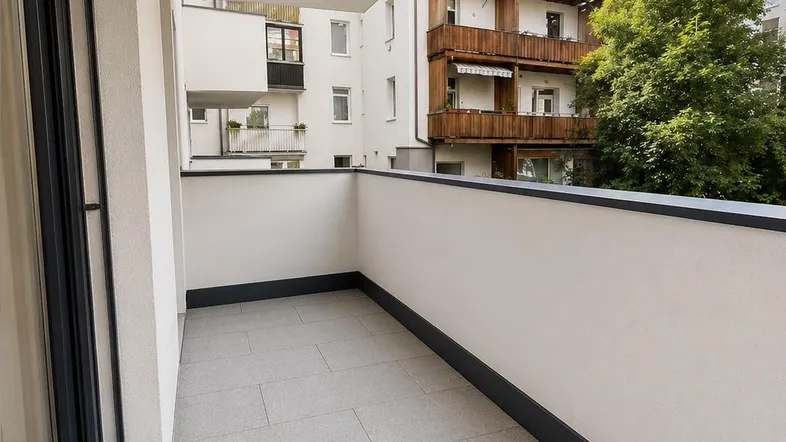 Heller Balkon mit Fliesenboden und Blick auf umliegende Gebäude und Bäume.