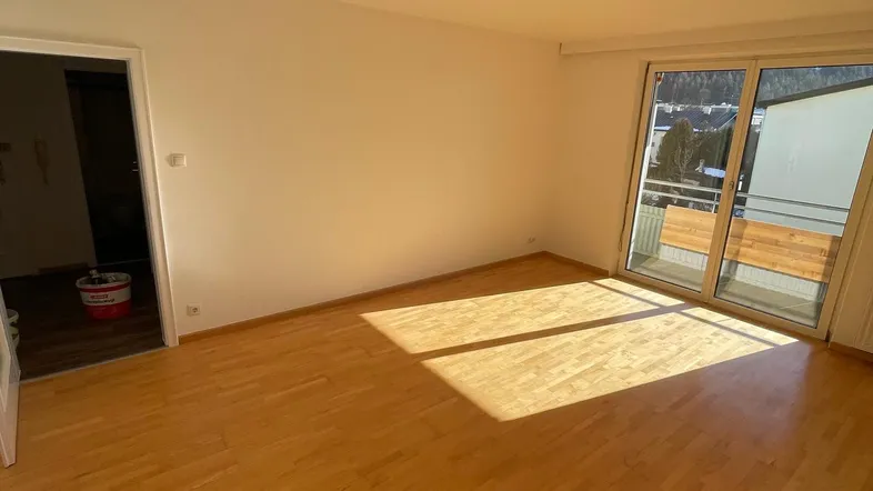 Helles Wohnzimmer mit Parkettboden und Zugang zu einem sonnigen Balkon, ideal für entspannte Stunden.