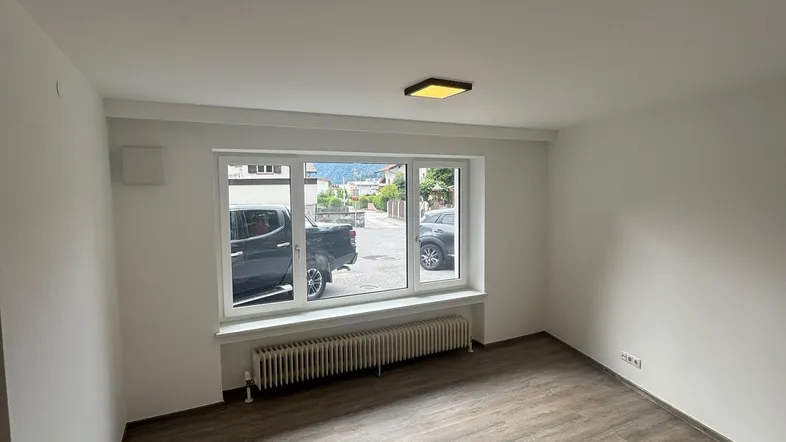 Helles, leeres Zimmer mit Laminatboden und Blick auf die Straße, bereit zur Einrichtung.