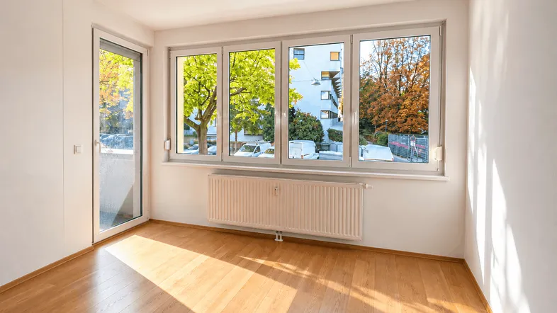 Helles Zimmer mit Holzboden, großen Fenstern und Zugang zu einem Außenbereich.