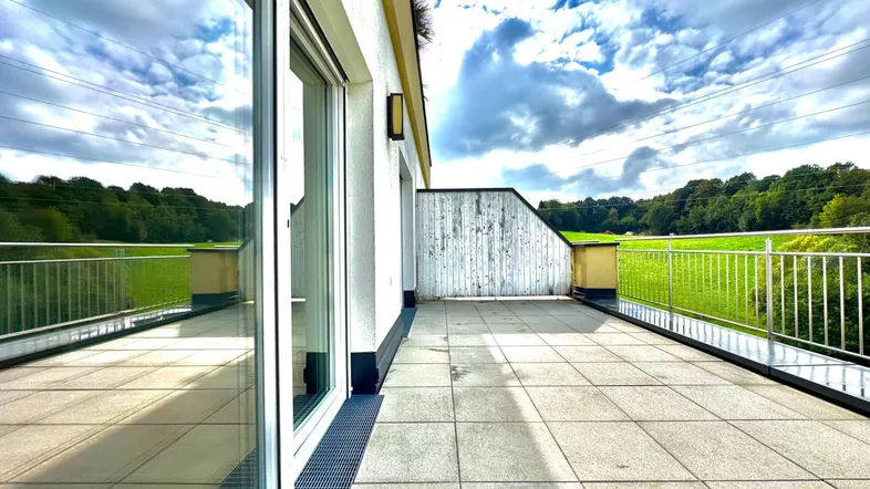 Große geflieste Terrasse mit weitem Blick ins Grüne unter blauem Himmel.