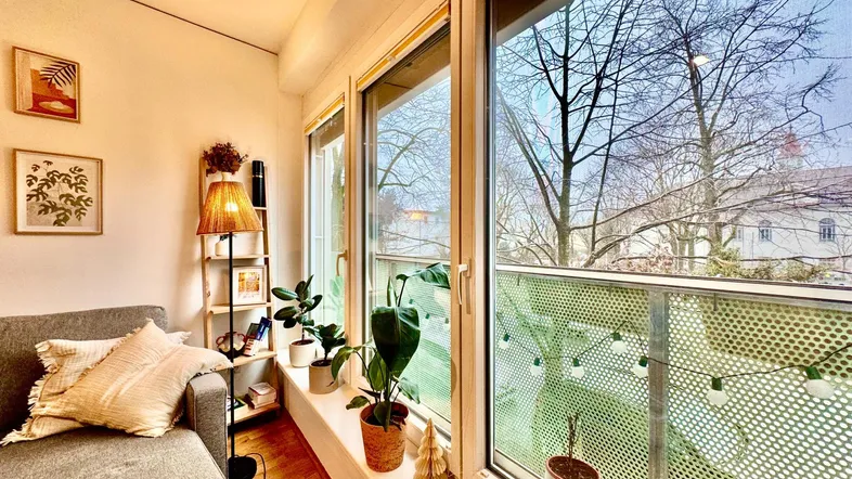 Helles Wohnzimmer mit gemütlichem Sofa, Pflanzen und Zugang zum Balkon mit Blick ins Grüne.