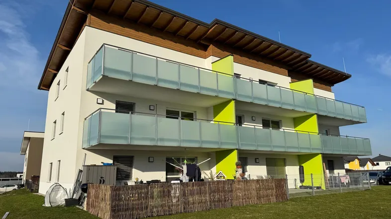 Modernes Mehrfamilienhaus mit weißer Fassade, grünen Akzenten und Balkonen unter blauem Himmel.
