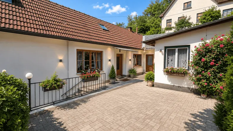 Vorderansicht des Hauses mit gepflastertem Hof und blühenden Pflanzen unter blauem Himmel.