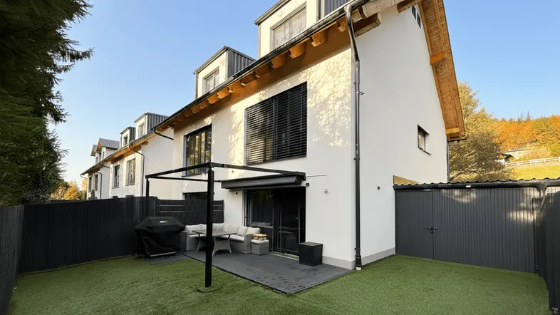 Moderne Reihenhaus-Rückseite mit gepflegtem Garten, Terrasse und gemütlicher Sitzecke.