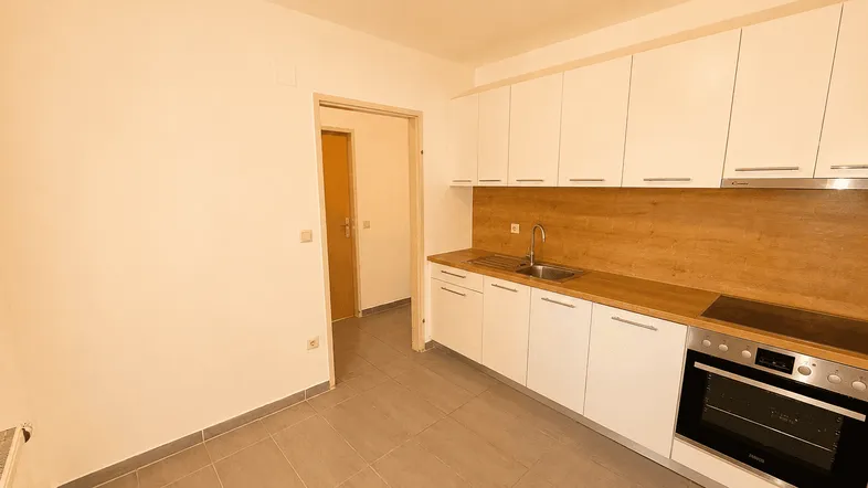 Moderne Küche mit weißen Schränken, Holzarbeitsplatte, integriertem Backofen und Induktionskochfeld.