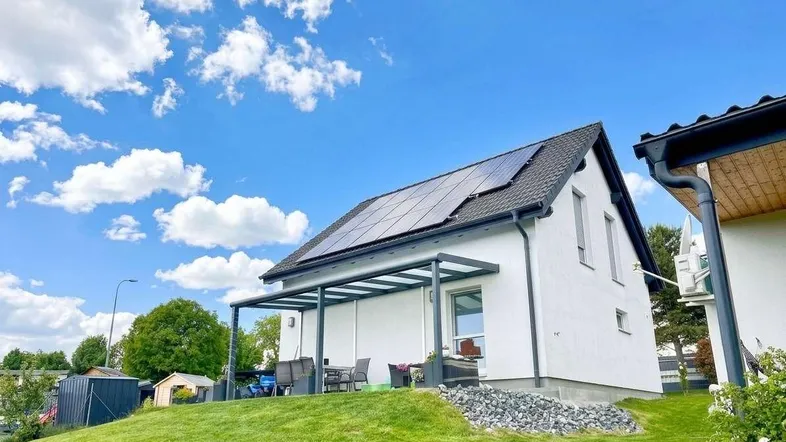 Modernes Einfamilienhaus mit überdachter Terrasse, Photovoltaikanlage auf dem Dach und gepflegtem Garten.