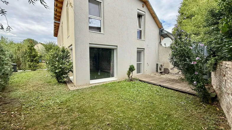 Seitlicher Blick auf das Haus mit Rasenfläche und einer kleinen Holzterrasse im Gartenbereich.