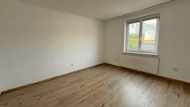Helles Zimmer mit Laminatboden und einem Fenster, ideal als Schlaf- oder Arbeitszimmer.