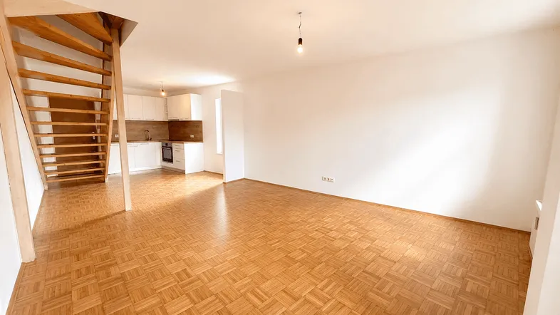 Weitläufiger Wohnbereich mit Parkettboden und offener Küche, verbunden durch eine Holztreppe.