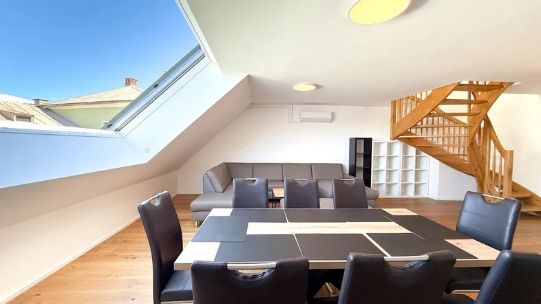 Geräumiger Wohn- und Essbereich mit Holzboden, Dachfenster und offener Holztreppe.