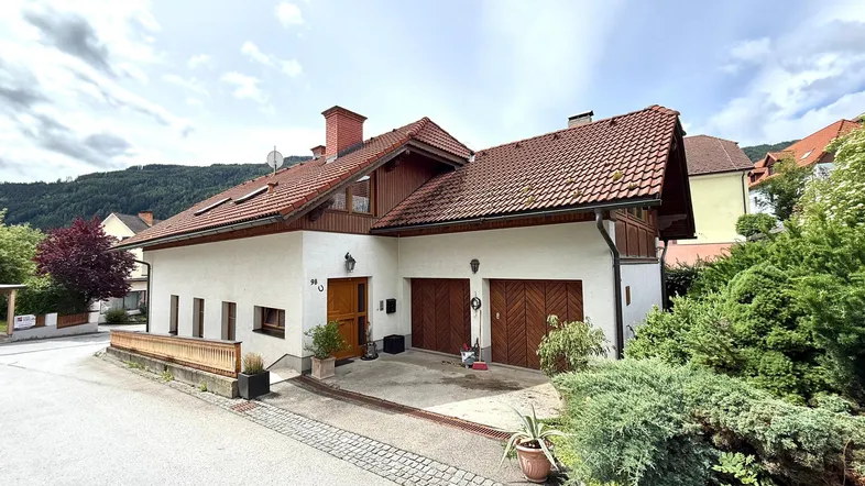 Charmantes Einfamilienhaus mit zwei Garagen und traditionellem Satteldach in grüner Umgebung.