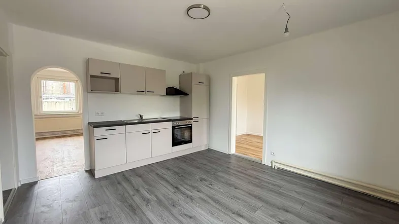 Helle Küche mit moderner Küchenzeile, integriertem Backofen und grauem Laminatboden in offenem Raum.