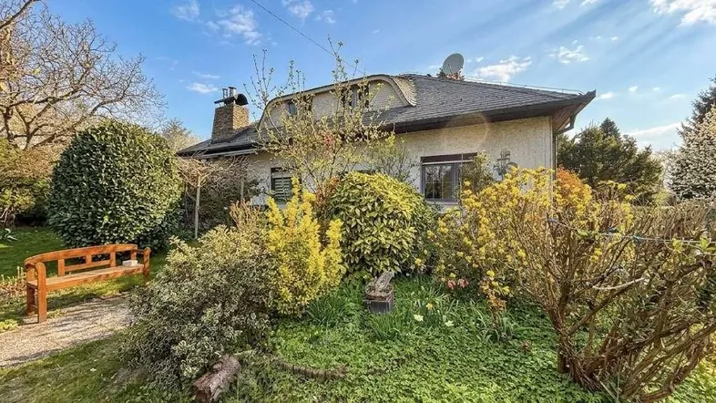 Charmantes Einfamilienhaus mit gepflegtem Garten und Sitzbank unter blauem Himmel.