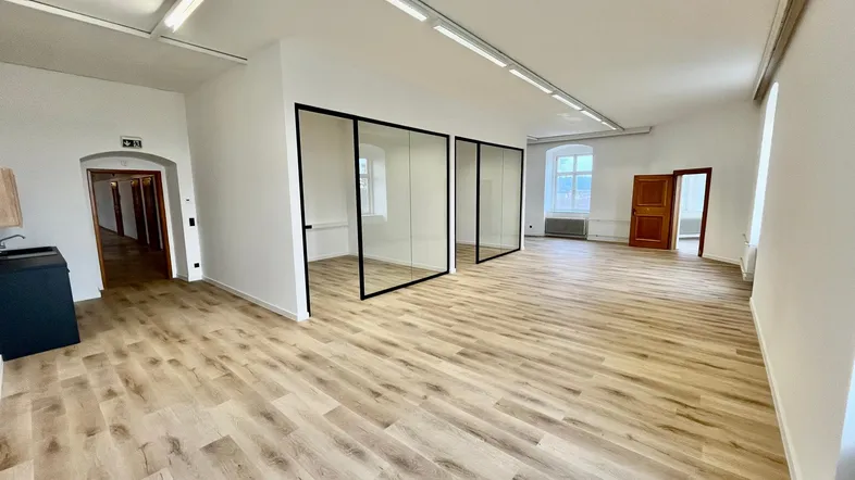 Geräumiger, heller Büroraum mit modernen Glasabtrennungen, Holzboden und integrierter Spüle.