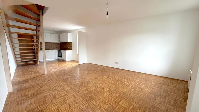 Heller offener Wohnbereich mit Parkettboden und integrierter Küche, verbunden durch eine Holztreppe.
