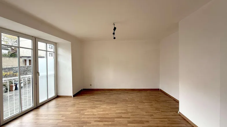 Helles, leeres Zimmer mit Laminatboden und großen Fenstern, die viel Tageslicht hereinlassen.