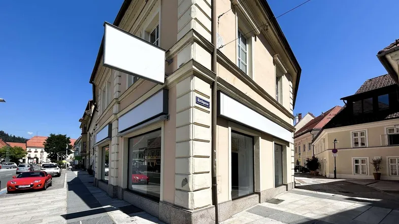Gebäude an einer Straßenecke mit großen Schaufenstern und leerstehenden Geschäftsflächen im Erdgeschoss.