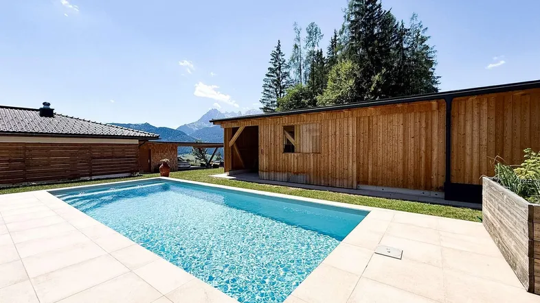 Außenbereich mit großem Pool, umgeben von einer Terrasse und Blick auf die Berge.