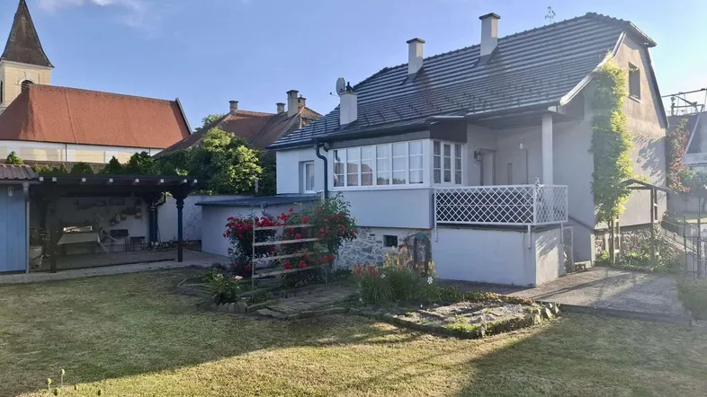 Großzügiger Gartenbereich mit Rasenfläche, Blumenbeeten und Blick auf die Kirche im Hintergrund.