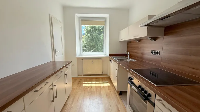 Helle Küche mit Holzoptik-Arbeitsplatten, Einbaugeräten und Fenster mit Blick ins Grüne.