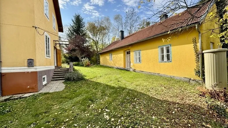 Zwei gelbe Gebäude mit roten Dächern und einem grünen Garten unter blauem Himmel.