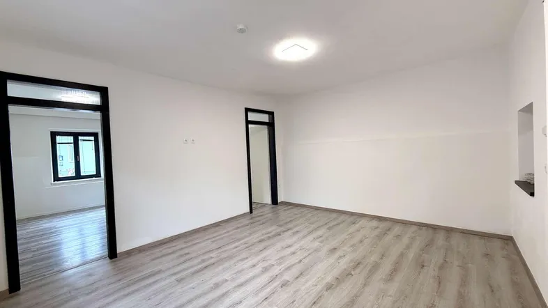 Helles, leeres Zimmer mit Laminatboden und weißen Wänden, bereit zur individuellen Gestaltung.