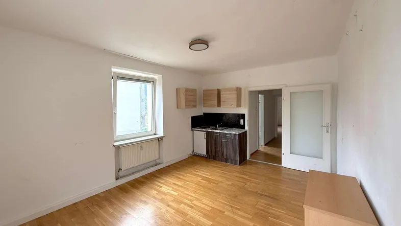 Helles Wohnzimmer mit Parkettboden und einer kleinen integrierten Küchenzeile.