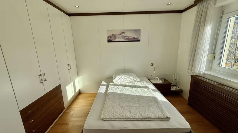 Helles Schlafzimmer mit Einzelbett, Einbauschränken und Holzboden, gut beleuchtet durch das Fenster.