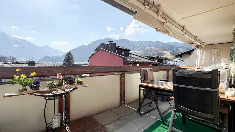 Geräumiger Balkon mit Holzbodenfliesen, Sitzgelegenheiten und einem weiten Blick auf die umliegende Berglandschaft.
